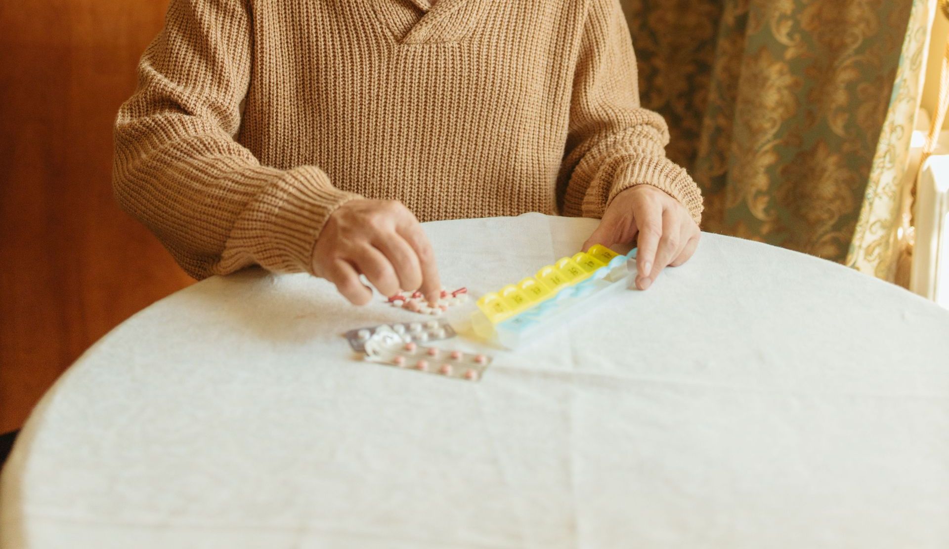 Elderly man with glasses arranging pills in a daily organizer at home.